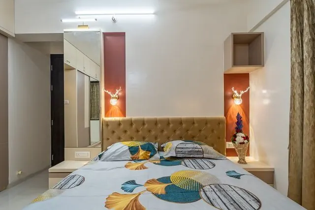A bedroom with an upholstered headboard and illuminated bedside niches.